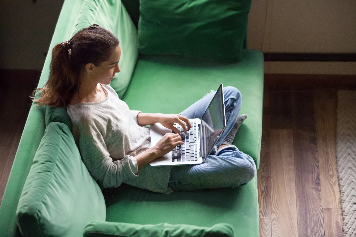 A student working on a laptop on a green sofa
